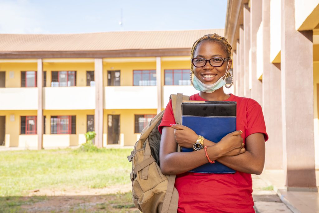 young african female student with facemask holding her textbooks campus area scaled 1